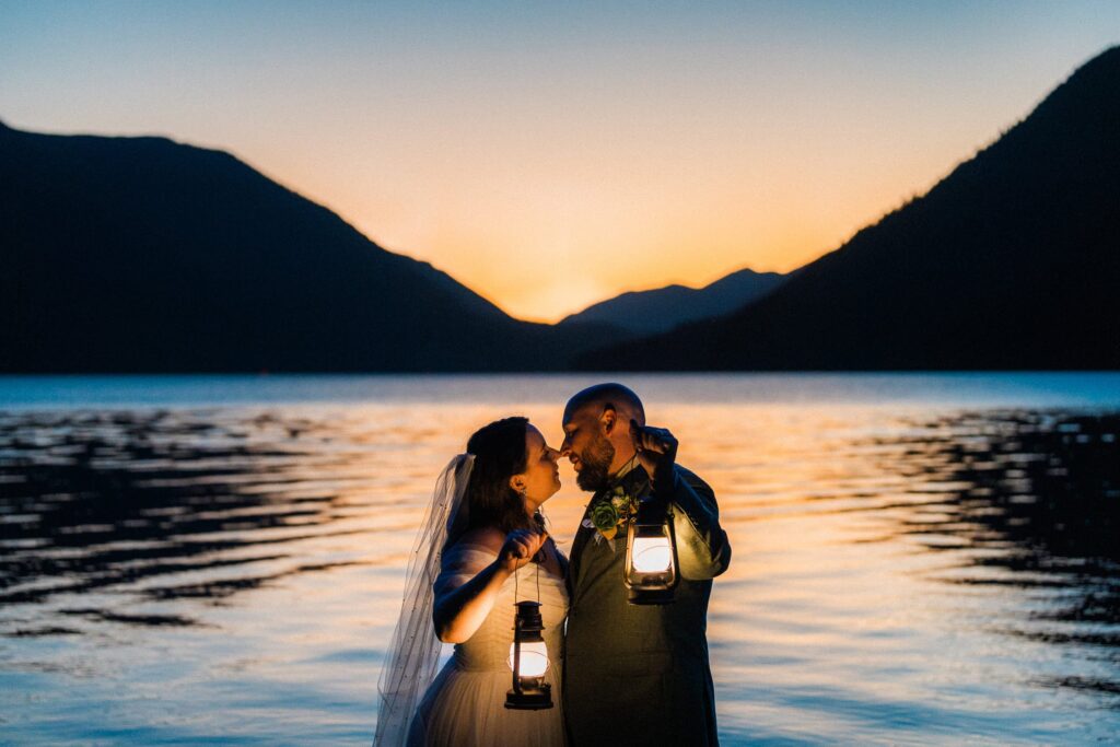 couple holding lanterns at sunset in wedding attire at Lake Crescent