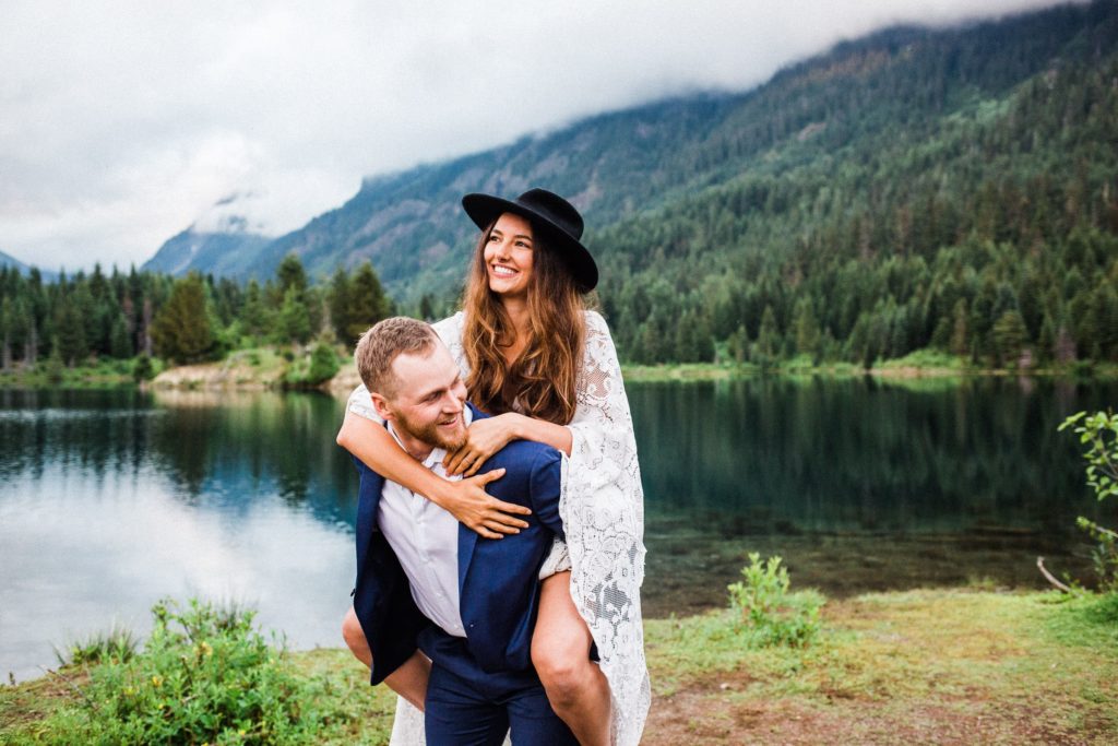 groom giving bride a piggy back ride in the mountains