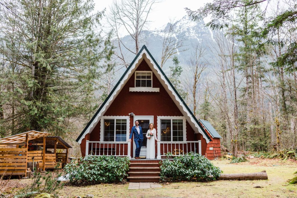 Couple standing on the steps of their red A-Frame cabin for their elopement. 