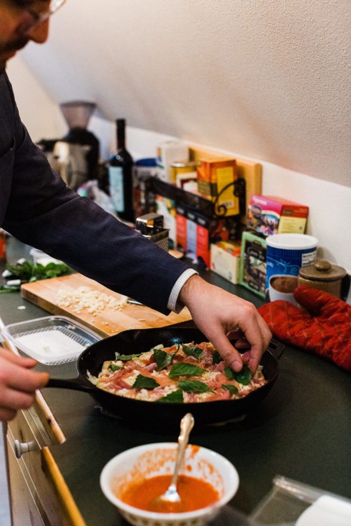 man adds basil to the top of a pizza
