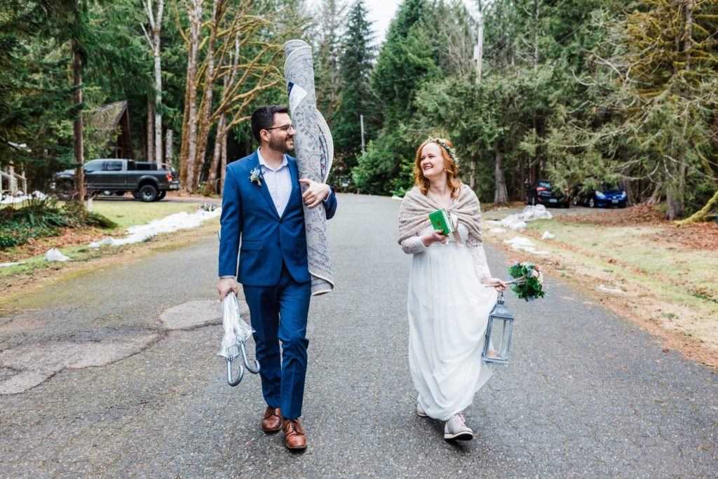 couple walks in the middle of the road carrying elopement ceremony decor.