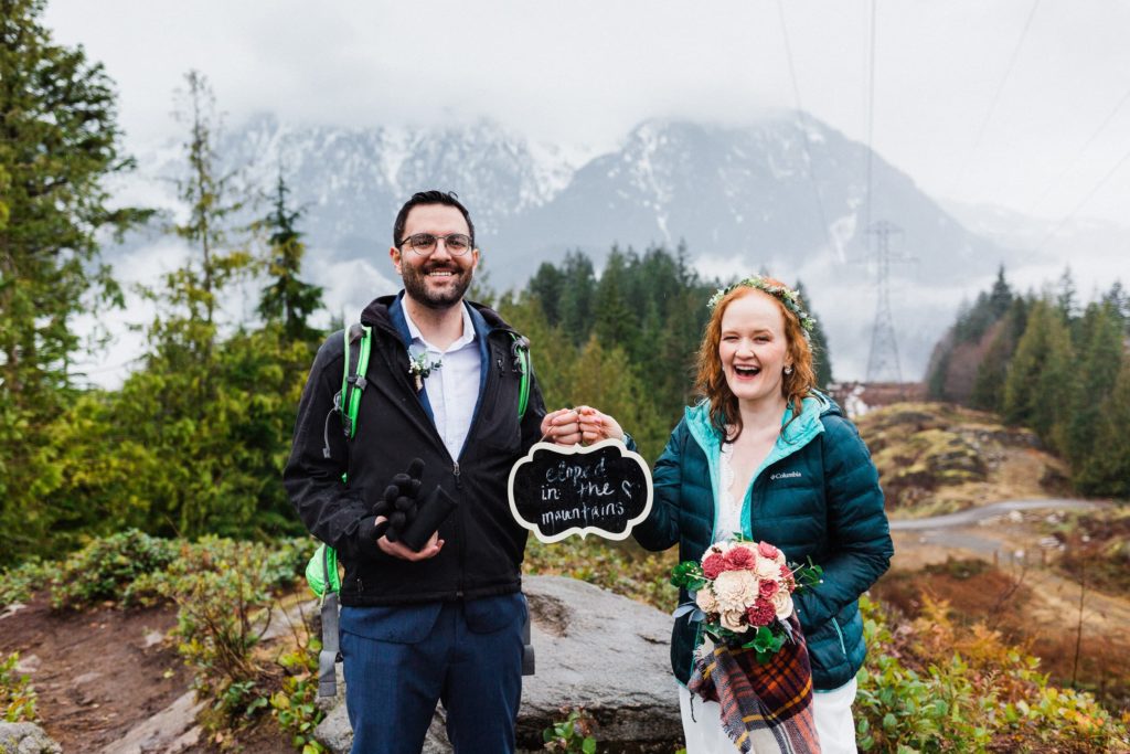 couple holding a sign saying "eloped in the mountains"