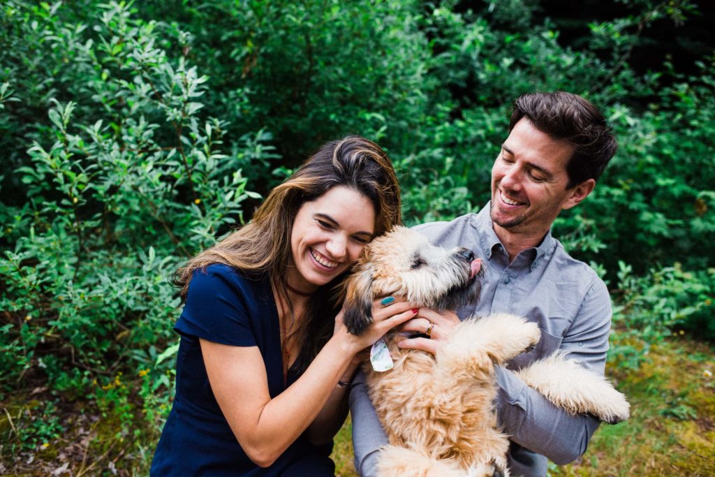 man and woman cuddling a dog with tongue sticking out. 