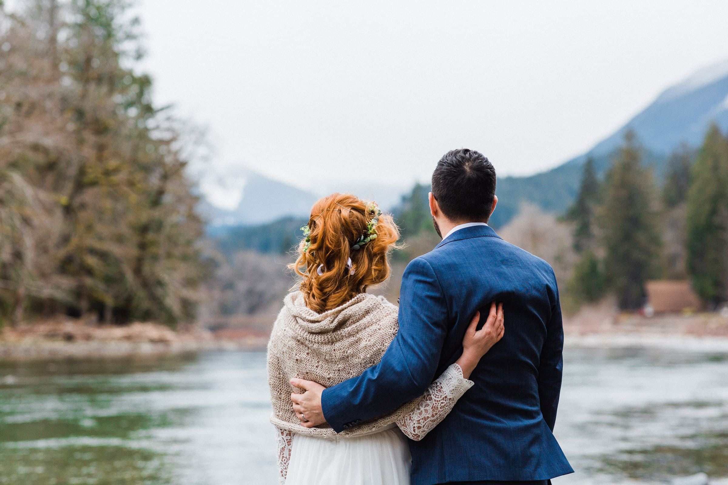 couple with backs to camera, looking over a river in the mountains