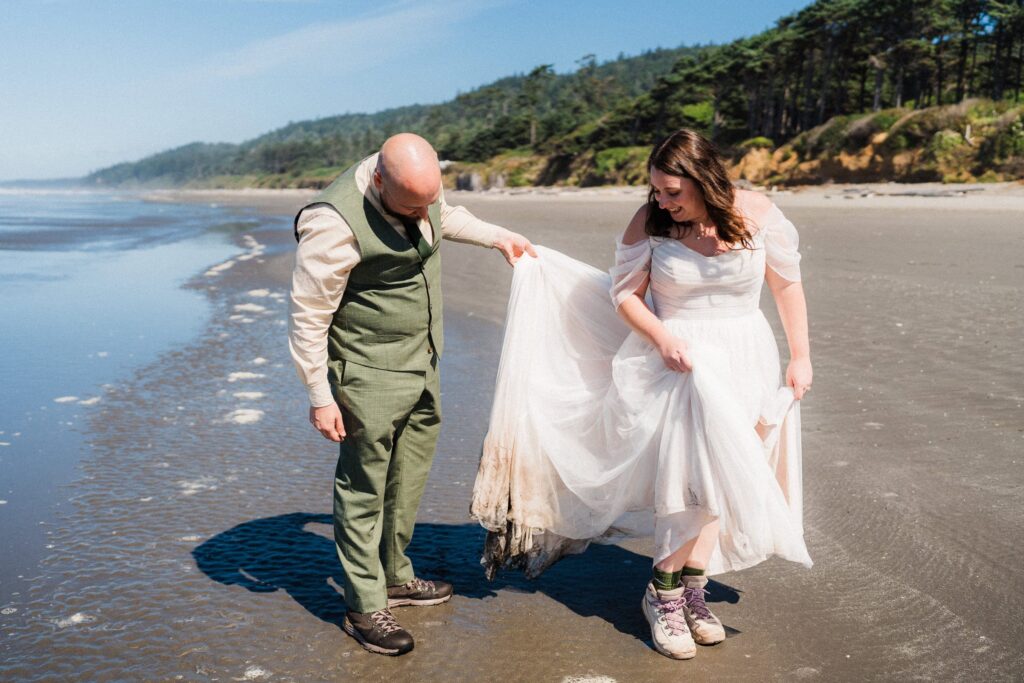 couple looking at dirty wet wedding dress on the beach in Washington