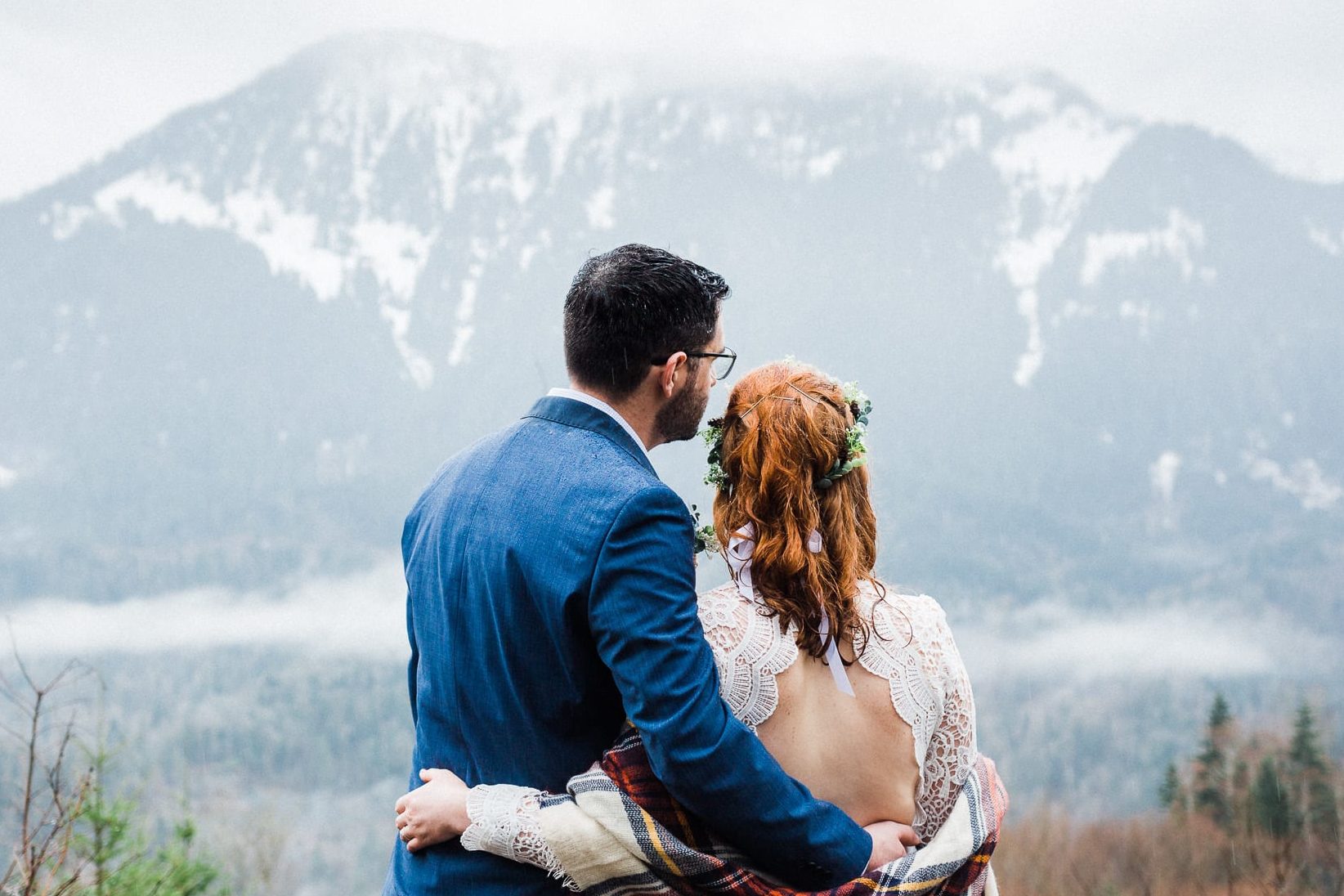couple dressed in wedding attire looking at the view of mountains in front of them.