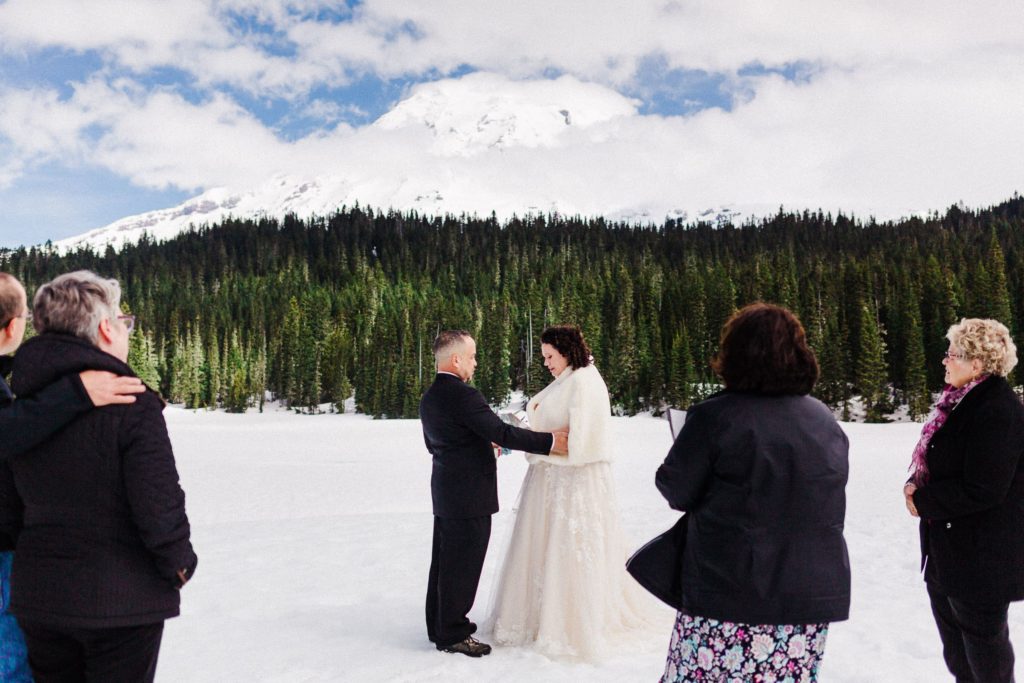 couple in wedding attire during an elopement ceremony with mount rainier peaking through clouds in the background