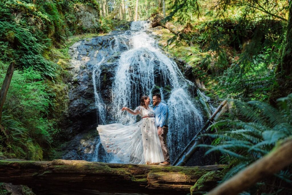 a bride throwing her dress and smiling at her partner in front of a waterfall during her San Juan Islands Elopement.