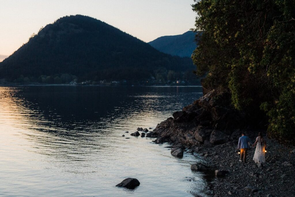a couple holding lanterns on the shore of their Orcas Island Elopement with mountains in the background.