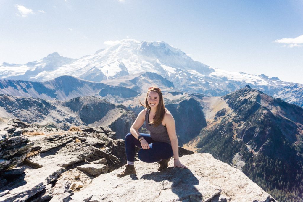 girl crouching on rock with mount rainier in the background on a sunny day