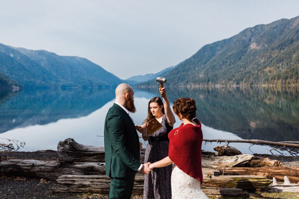 wedding couple getting a blessing from  their officiant holding Thor's hammer, standing next to an alpine lake