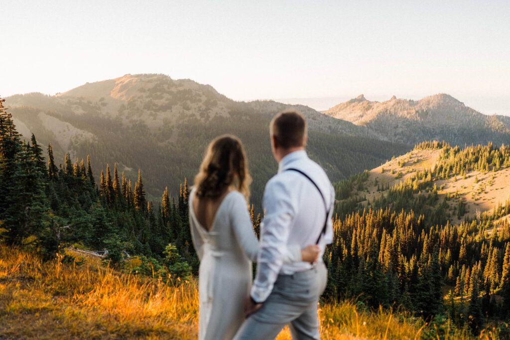 an eloping couple admiring the view of the sun glowing over the mountains in Washington
