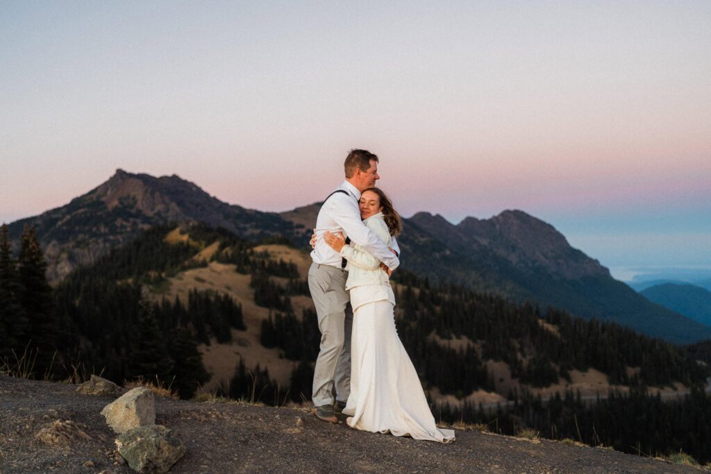 a couple embracing during their Olympic National Park Elopement amidst the mountains under cotton candy skies.