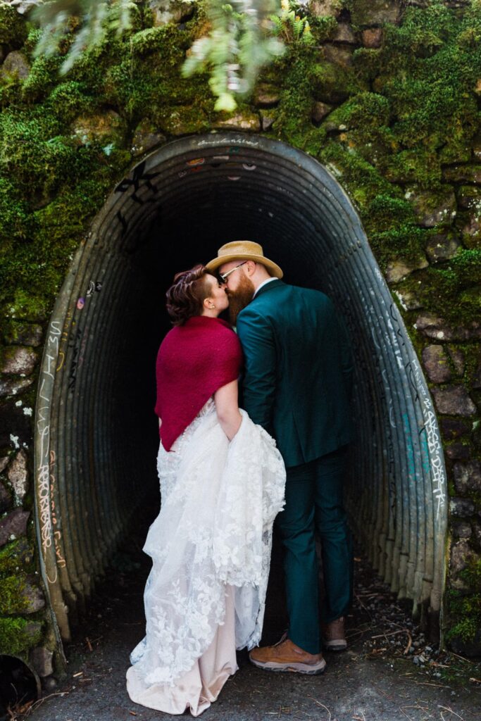 couple in wedding attire kissing in a tunnel surrounded by green moss