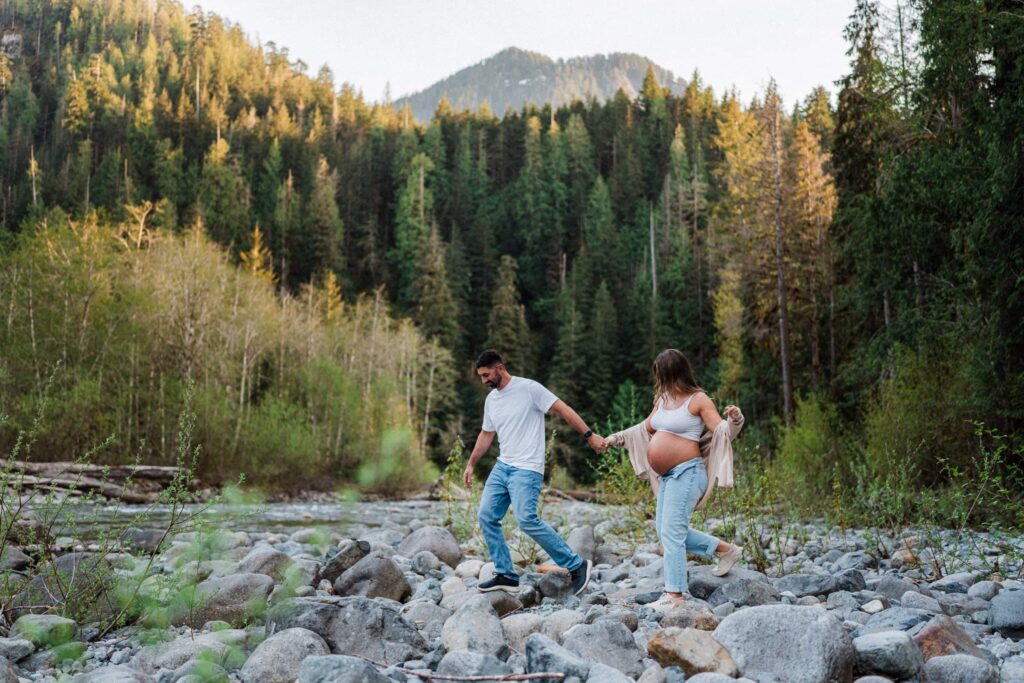 couple climbing on rocks below the mountains for their sunset Snoqualmie Valley Maternity session.
