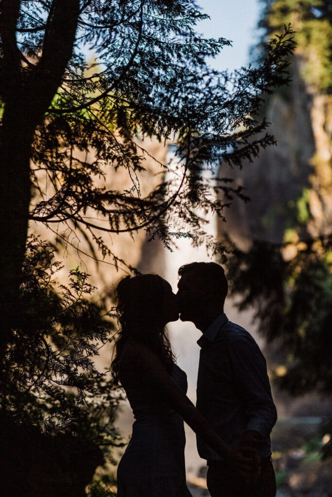 a silhouetted couple with a roaring waterfall behind them in North Bend, WA