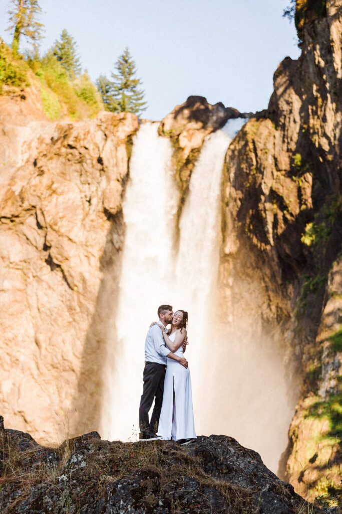 a couple standing on a rock in front of Snoqualmie Falls for their summer elopement.